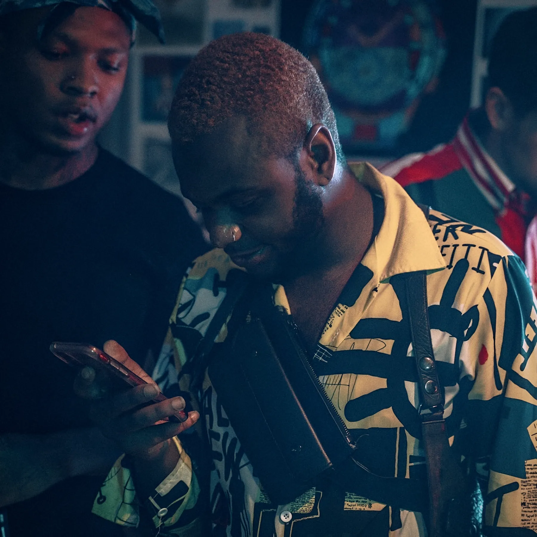 Bobby Brown Jr. in a yellow-and-black shirt looking down at his phone, a friend standing behind him